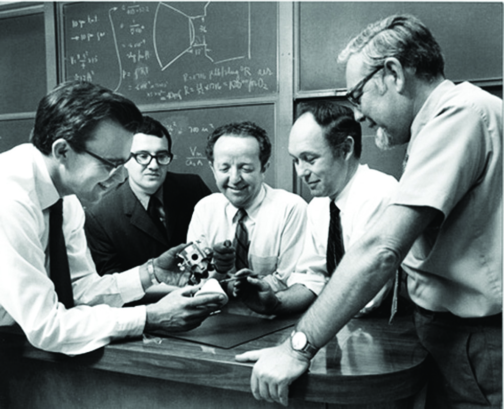Five UTIAS Professors in a classroom gathered around a metal device
