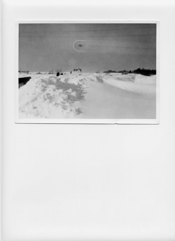 Black and white photo of a black smudge in the sky over a snowy bank