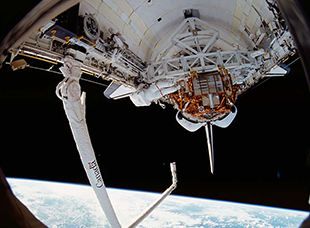 Canadarm extending from the International Space Agency, orbiting over the earth